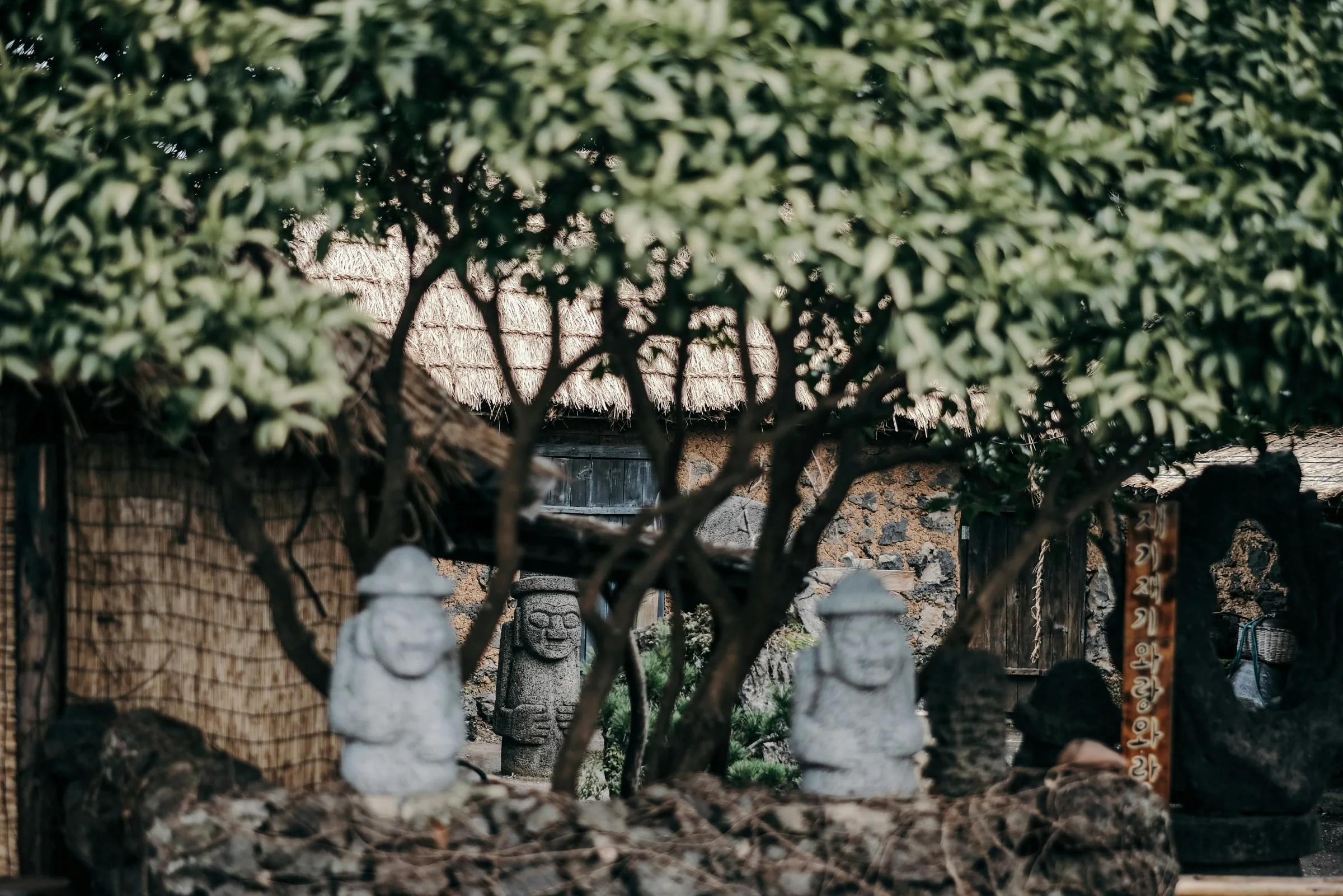 Traditional Jeju stone walls, dol hareubang statues, and a thatched house